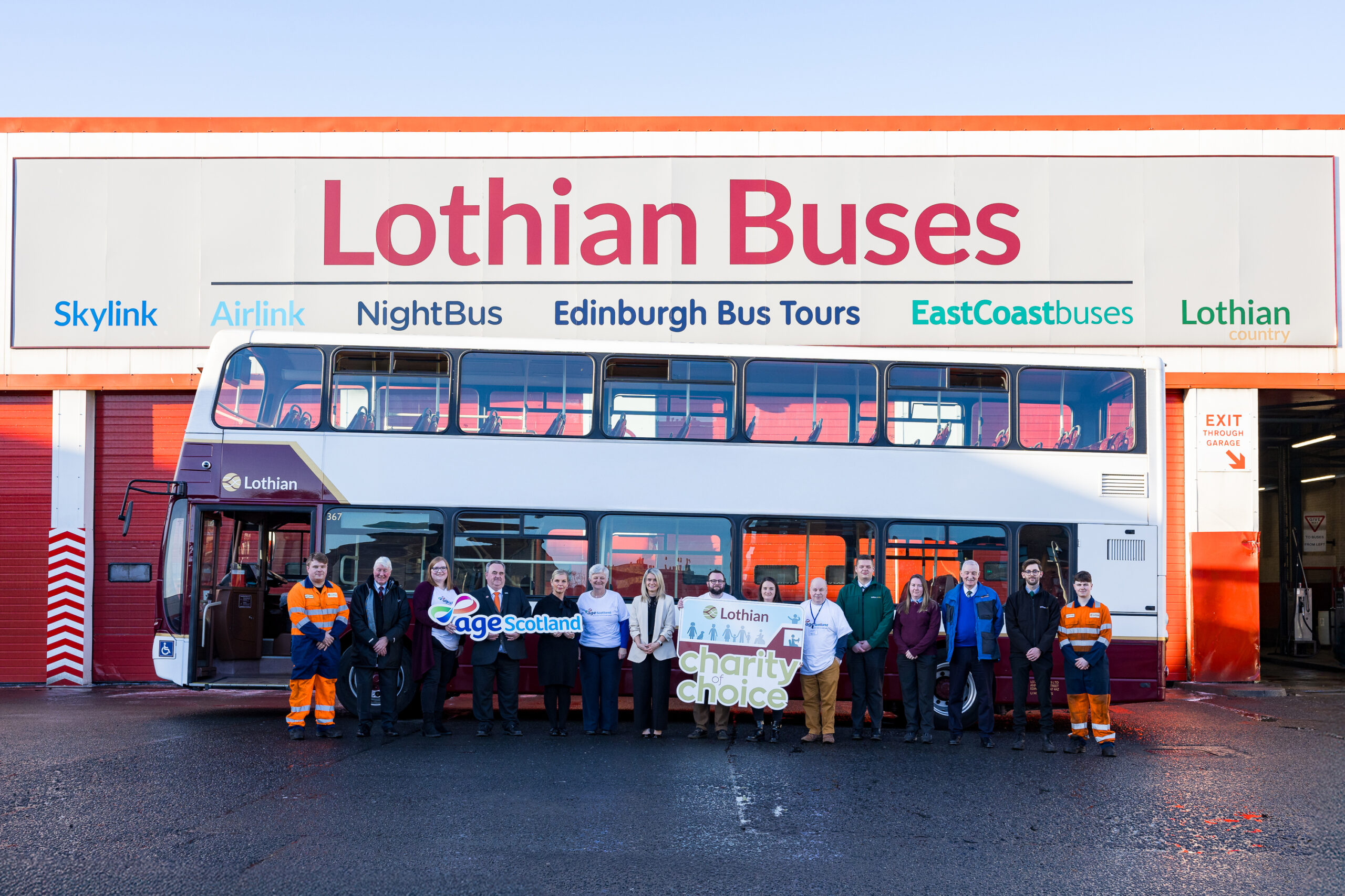 Age Scotland and Lothian Buses staff members stand in front of a Lothian bus at the garage, holding logos an signs to mark the launch of the partnership.